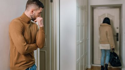 Zamyślony mężczyzna stojący w drzwiach, podczas gdy kobieta z torbą wychodzi z mieszkania – prawnik od rozwodów